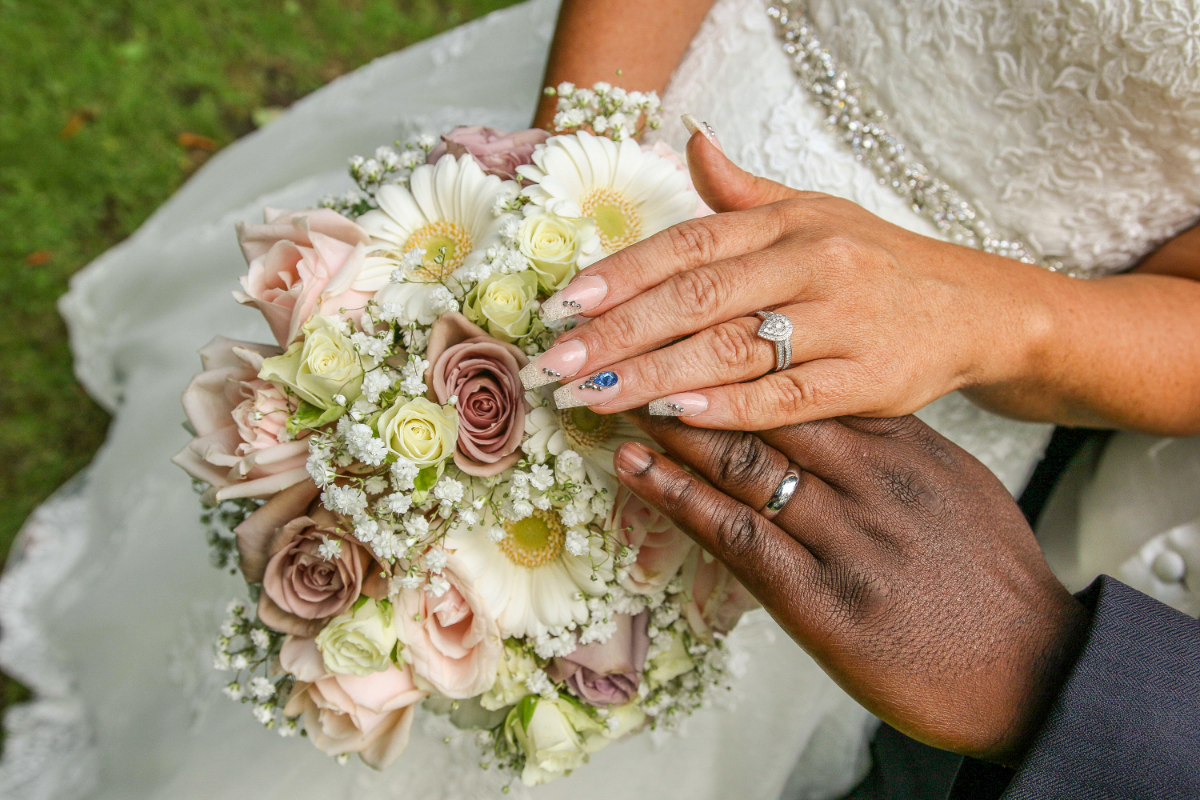 bride and groom hands placed on top of bouquet showing rings on wedding finger